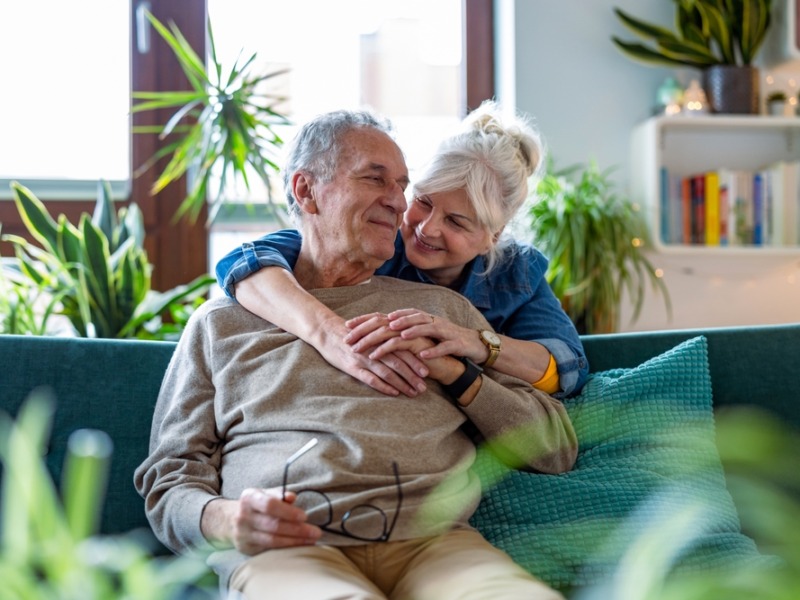 Portrait Of A Happy Senior Couple Sitting On Sofa At