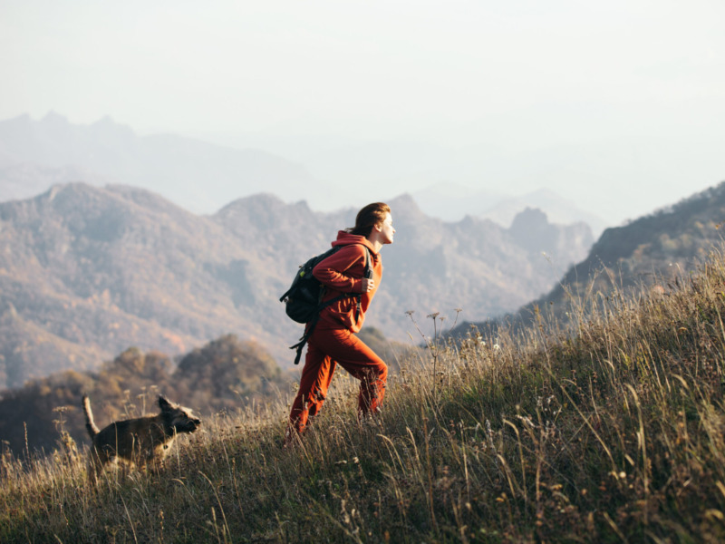 Beautiful woman traveler climbs uphill with a dog on a backgroun